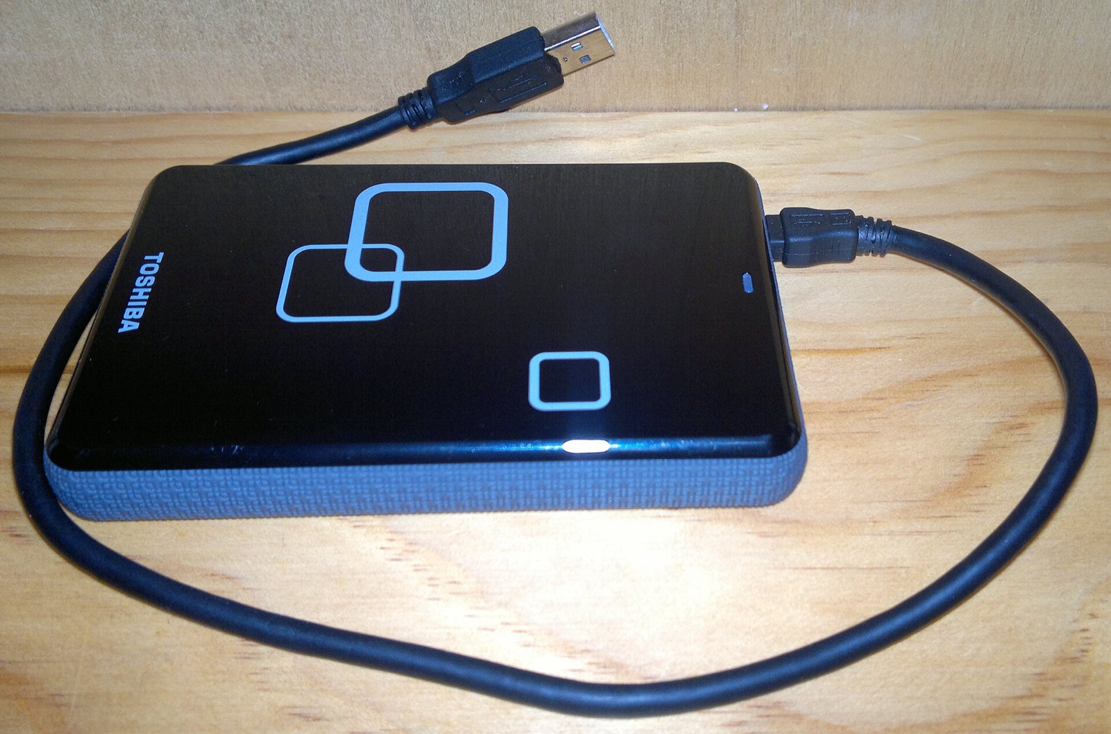 A black Toshiba external hard drive with its cable, on a wooden table.